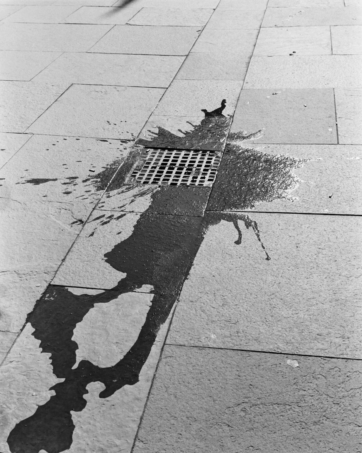 Black and white photograph of a stain on the sidewalk that looks like a human figure