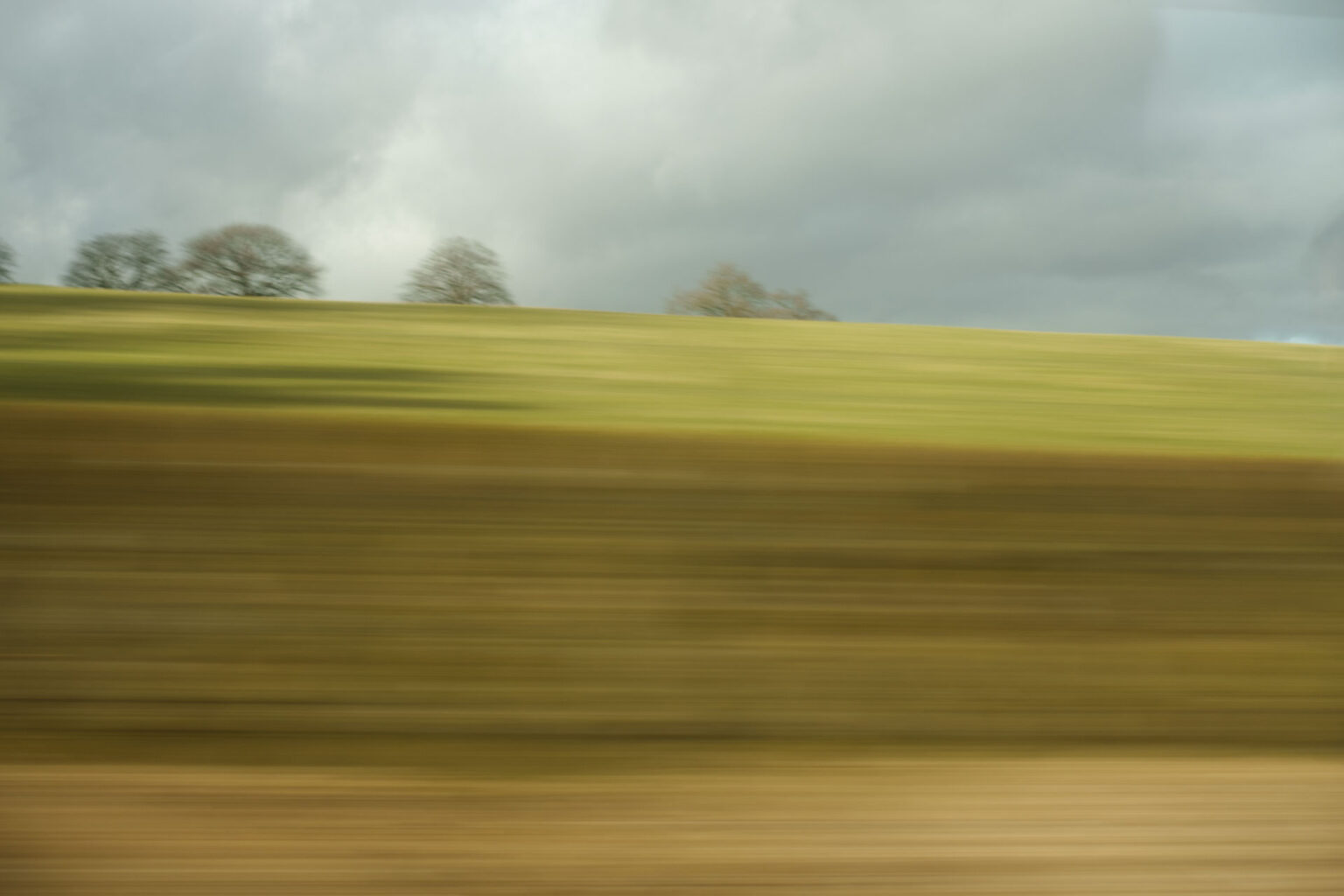 A blurry landscape image shot through a window on a moving train