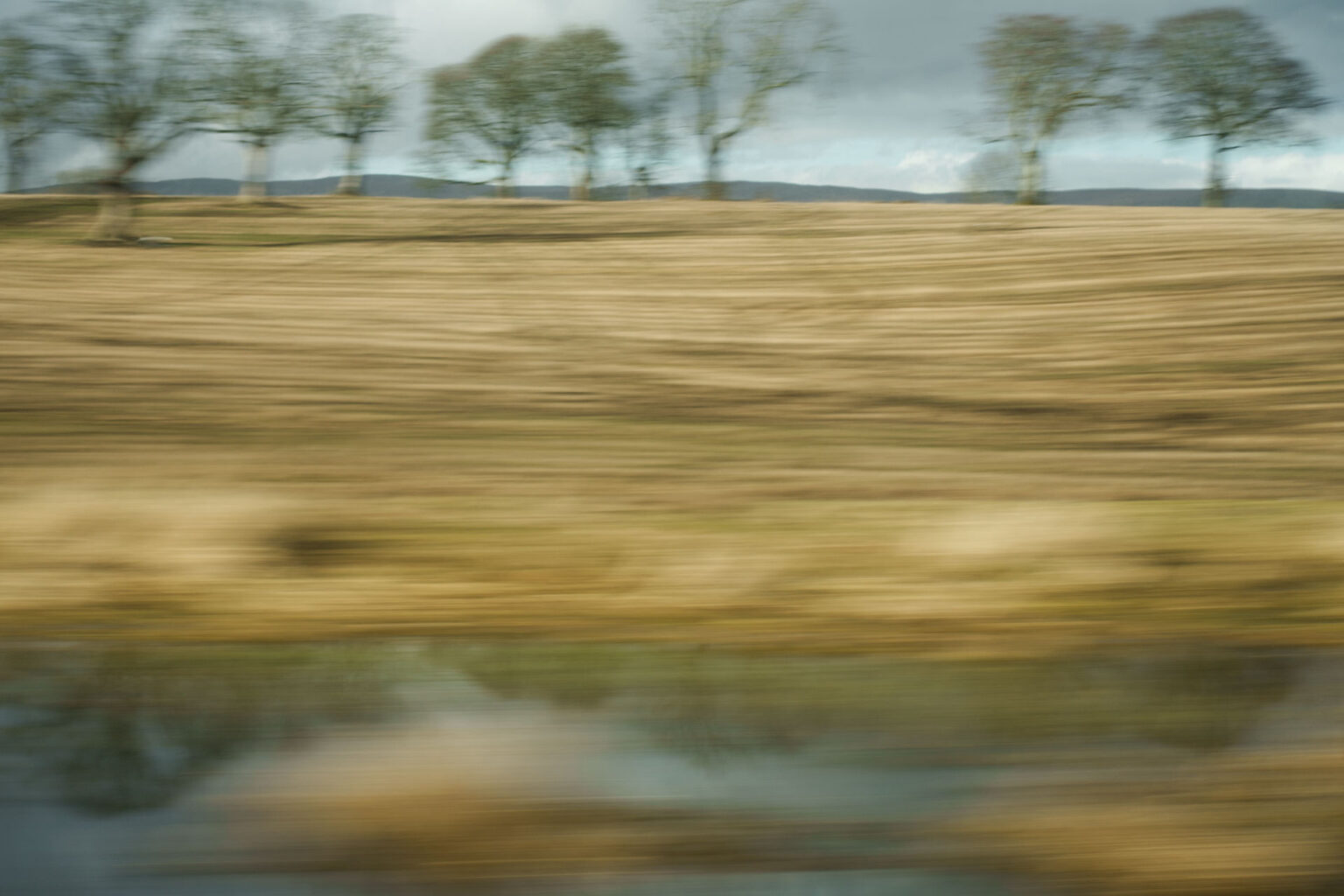 A blurry landscape image shot through a window on a moving train