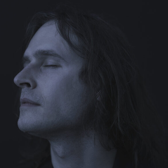 Somber portrait of Błażej, sharp edges, delicate blue light. His eyes are closed.
