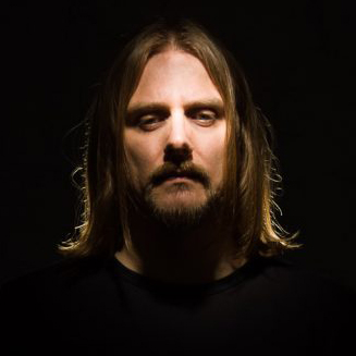 Portrait of Mariusz Duda, singer of the band Riverside. His face is lit up but the rest of the photograph is in the shadow.