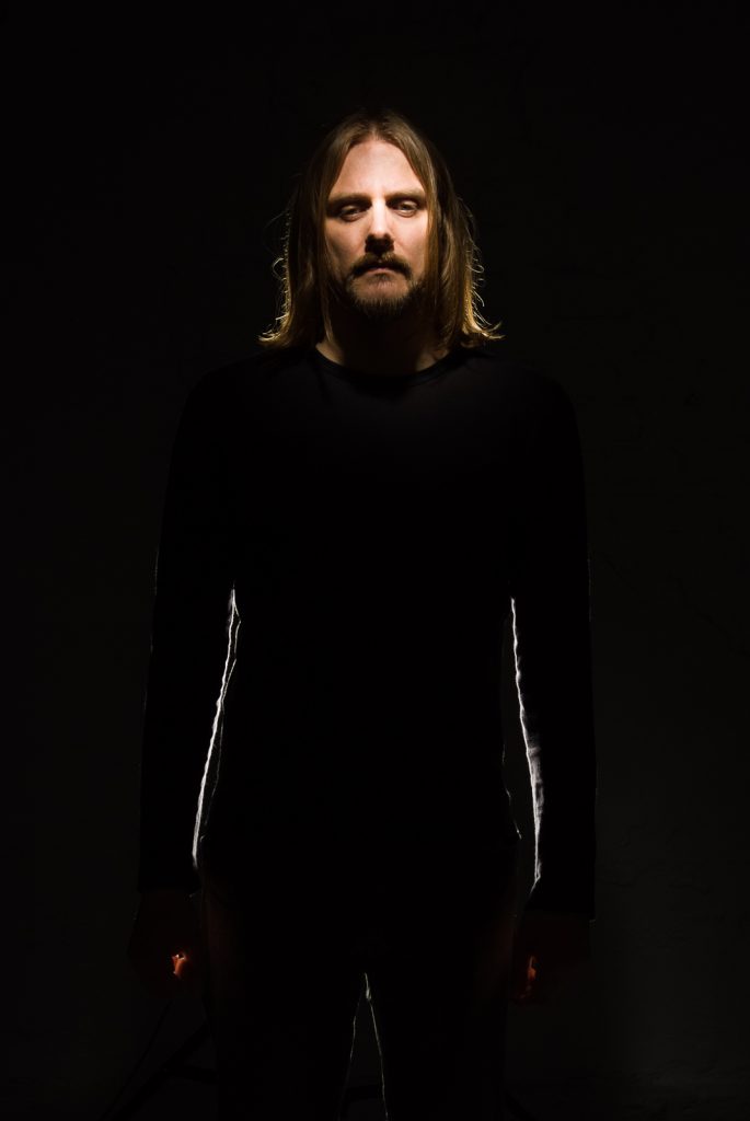 Portrait of Mariusz Duda, singer of the band Riverside. His face is lit up but the rest of the photograph is in the shadow.