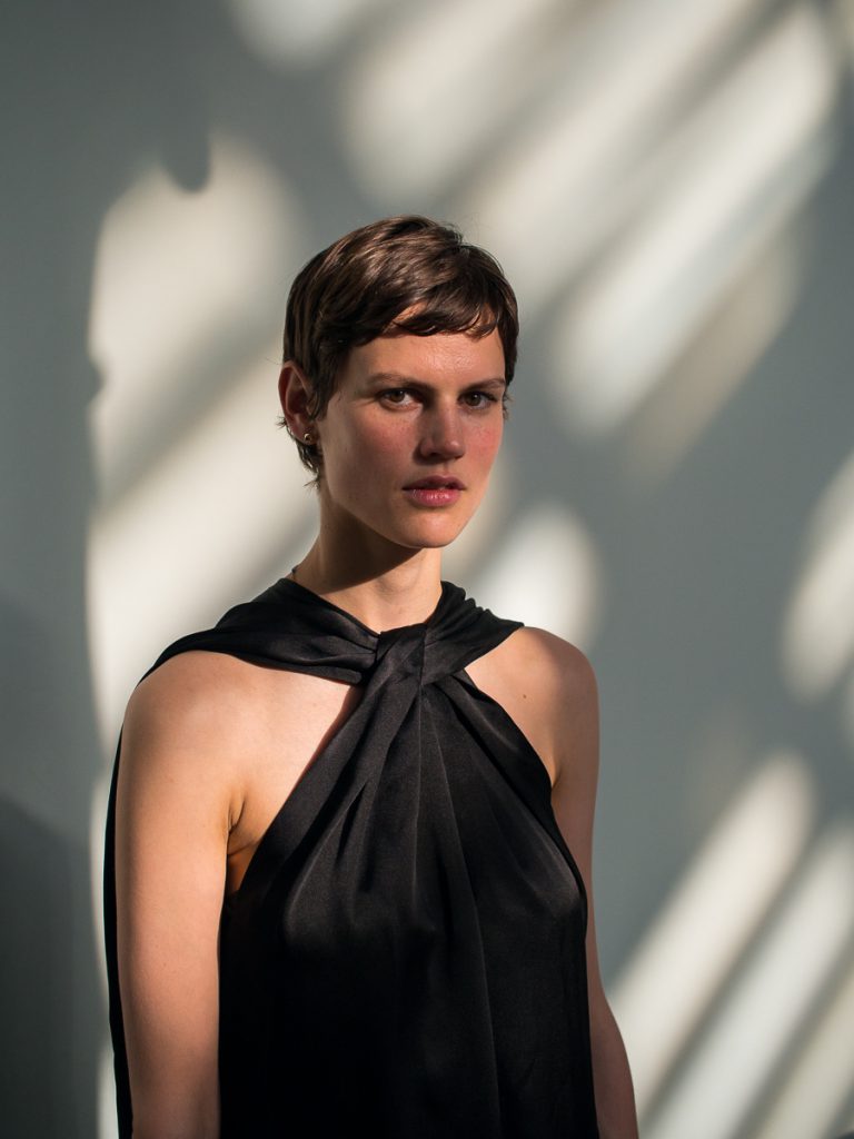 Portrait of Saskia de Brauw, an international fashion model, in a black dress on a sunlit wall.